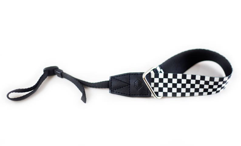 May include: Black and white checkered camera strap with a black leather adjustable section and a silver metal loop.