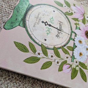 May include: A canvas painting featuring a vintage family scale design with a floral arrangement. The scale is painted in green and cream, with the words "Family Scale" visible. Pink and white flowers and green leaves surround the scale, set against a pale pink background.