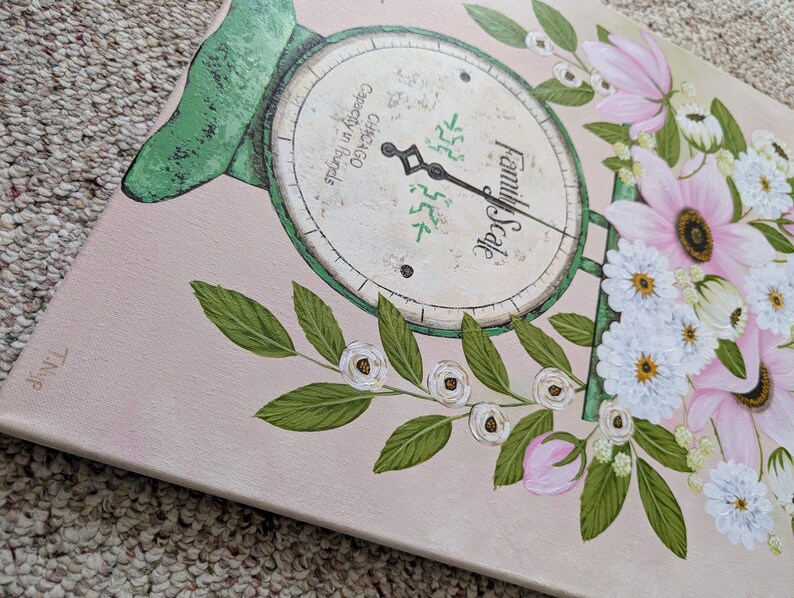 May include: A canvas painting featuring a vintage family scale design with a floral arrangement. The scale is painted in green and cream, with the words "Family Scale" visible. Pink and white flowers and green leaves surround the scale, set against a pale pink background.