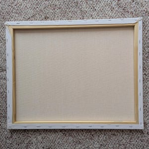 May include: Back of a rectangular canvas stretched over a wooden frame. The canvas is a light beige color, and the frame is a natural wood tone. The canvas is stapled to the wooden frame. The edges of the canvas are white.
