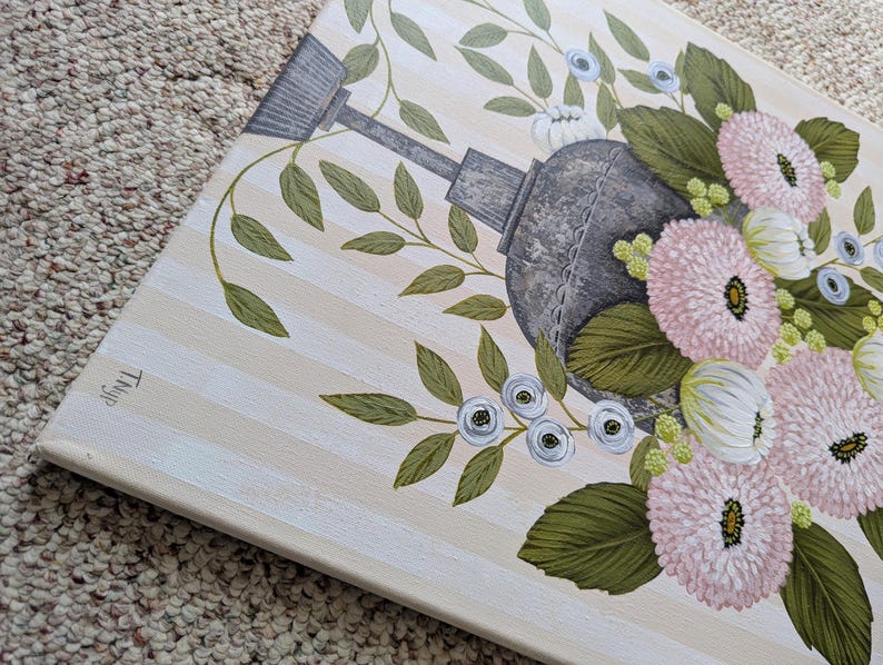 May include: A floral painting featuring a gray watering can surrounded by pink and white flowers, green leaves, and small blue flowers. The background has vertical beige and white stripes. The artwork is on a canvas.