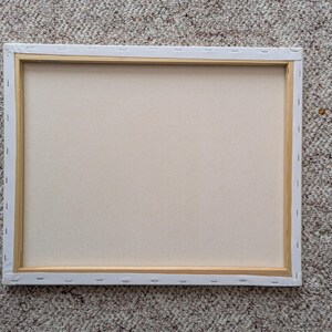 May include: A rectangular canvas stretched over a wooden frame, viewed from the back. The canvas is a light beige color, and the wooden frame is visible around the edges. The canvas is stapled to the frame.