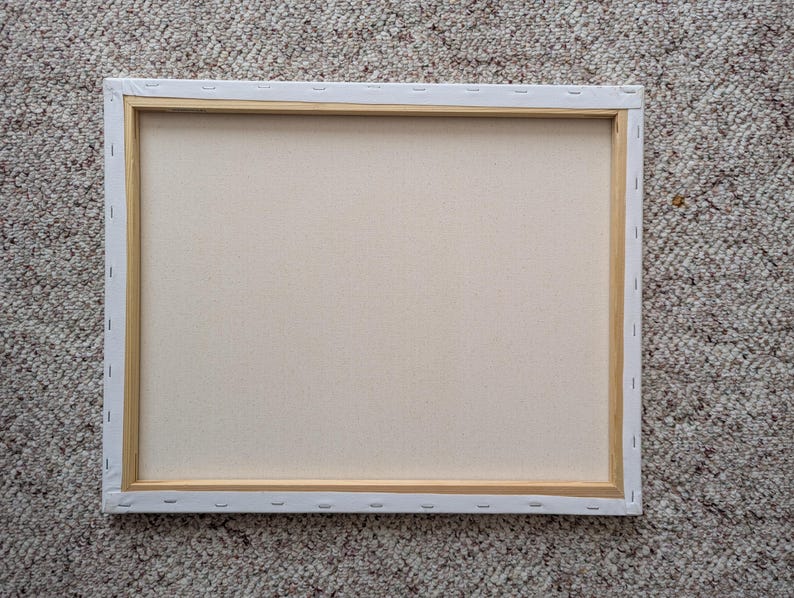 May include: A rectangular canvas stretched over a wooden frame, viewed from the back. The canvas is a light beige color, and the wooden frame is visible around the edges. The canvas is stapled to the frame.