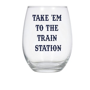 May include: A clear glass wine glass with the text "TAKE 'EM TO THE TRAIN STATION" printed in dark blue.