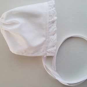 Può includere: Cappellino bianco per neonato con bordo in pizzo e nastro di raso bianco.