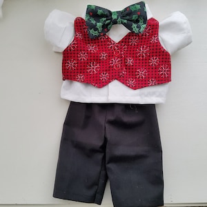 May include: A festive doll outfit featuring a white collared shirt, black shorts, and a red vest with a snowflake pattern. A green bow tie with holly accents completes the holiday ensemble.