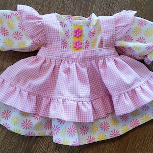 Könnte beinhalten: Ein rosa-weißes Gingham-Kleid mit einem gelben und rosa floralen Überzug. Das Kleid hat einen Rüschenrock und Ärmel.