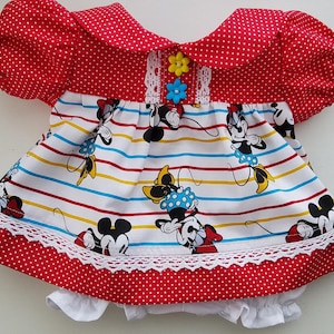 May include: A short-sleeved dress with a red and white polka dot bodice, collar, and hem. The skirt features a white background with horizontal stripes and a repeating cartoon mouse print. It includes white lace trim and two small flower-shaped buttons.