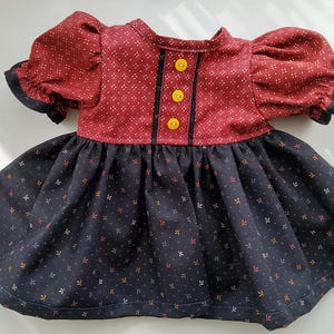 Könnte beinhalten: Ein kurzärmeliges Kleid mit einem dunkelroten Oberteil mit kleinem weißem geometrischen Muster und drei leuchtend gelben Knöpfen in der Mitte. Der Rock ist dunkelmarineblau mit einem Streumuster aus winzigen bunten Blattformen.