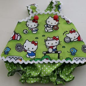 Peut inclure: Une barboteuse pour bébé vert citron avec un motif répétitif de personnages Hello Kitty pratiquant divers sports, notamment le baseball, le football et le badminton. Le vêtement est agrémenté d'une bordure en croquet blanc et deux boutons rouges.