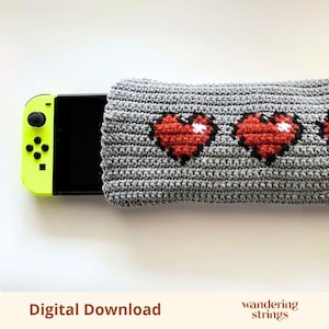 Può includere: Una custodia all'uncinetto grigia per console di gioco, caratterizzata da un motivo ripetuto di cuori pixelati rossi con riflessi bianchi. La custodia copre parzialmente una console di gioco nera con un controller giallo neon.