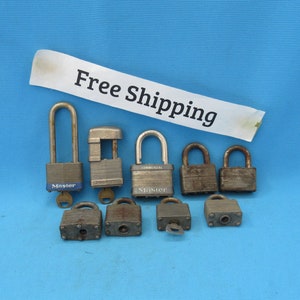 May include: A collection of vintage metal padlocks of various sizes and designs, some with keys. The locks are in shades of silver and gray, with visible wear and tear. The background is a solid blue.