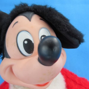 Peut inclure: Gros plan d'une peluche vintage de Mickey Mouse. Le jouet pr&eacute;sente un nez noir, des oreilles noires et une tenue rouge et blanche. Le visage est rose avec de grands yeux blancs et une expression souriante.