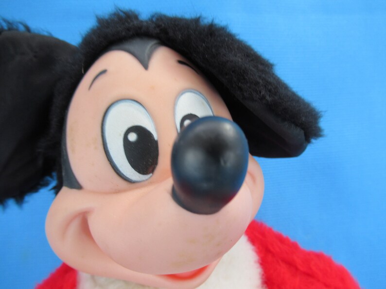 Peut inclure: Gros plan d'une peluche vintage de Mickey Mouse. Le jouet pr&eacute;sente un nez noir, des oreilles noires et une tenue rouge et blanche. Le visage est rose avec de grands yeux blancs et une expression souriante.