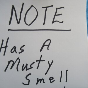 Peut inclure: Un post-it blanc avec le mot "NOTE" &eacute;crit en marqueur noir, soulign&eacute;. En dessous, la note dit "Has A Musty Smell!" sur un fond bleu.