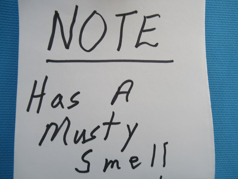 Peut inclure: Un post-it blanc avec le mot "NOTE" &eacute;crit en marqueur noir, soulign&eacute;. En dessous, la note dit "Has A Musty Smell!" sur un fond bleu.