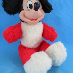 Peut inclure: Une peluche vintage de Mickey Mouse. La peluche pr&eacute;sente une t&ecirc;te noire avec de grandes oreilles, un visage rose et une tenue rouge et blanche. Le jouet est assis, les jambes tendues.