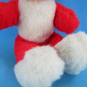 Peut inclure: Une poup&eacute;e en peluche vintage avec une tenue rouge et blanche. La poup&eacute;e a des cheveux noirs et un visage souriant. Le corps de la poup&eacute;e est rouge avec une poitrine blanche et des pieds blancs et duveteux. La poup&eacute;e est assise.