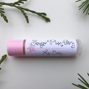 Könnte beinhalten: Ein rosa Lippenbalsam-Stift mit einem weißen Etikett, auf dem "Sugar Plum Fairy Lip Balm" steht.