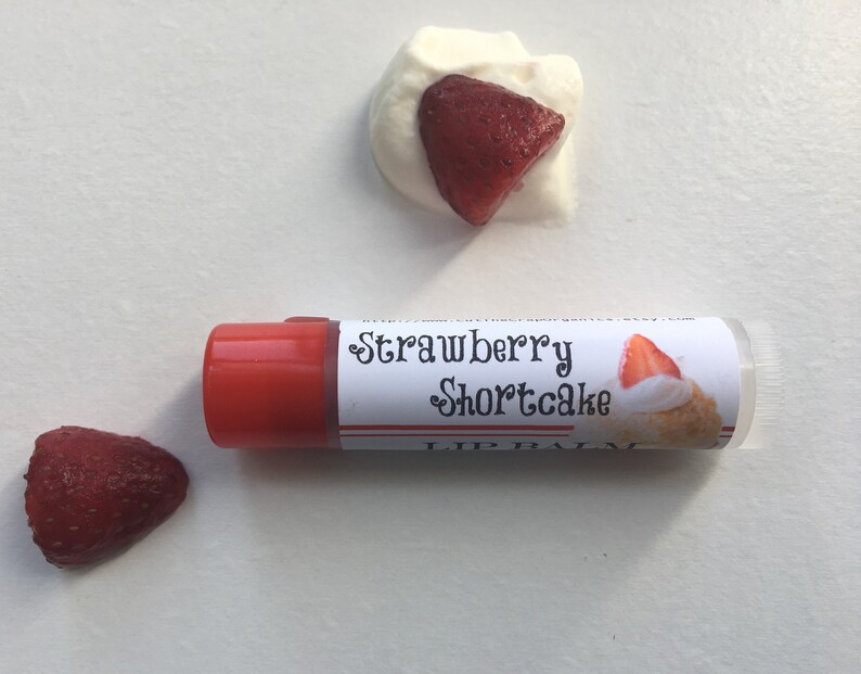 May include: A red and clear lip balm tube with a white label that says "Strawberry Shortcake Lip Balm". The label also features a small image of a strawberry shortcake dessert.