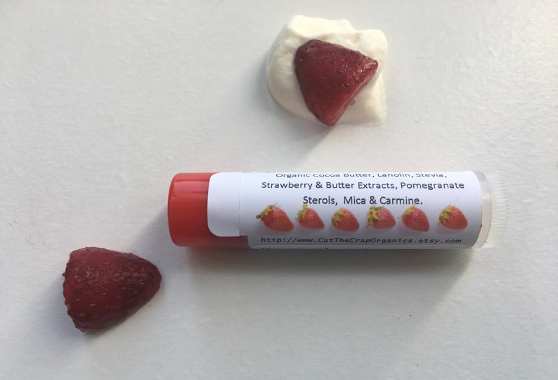 May include: A red lip balm tube with a white label that reads "Organic Cocoa Butter, Lanolin, Stevia, Strawberry & Butter Extracts, Pomegranate Sterols, Mica & Carmine." The label also includes a website address: "http://wwww.CutTheCrapOrganics.etsy.com". There are five small red strawberry images on the label.