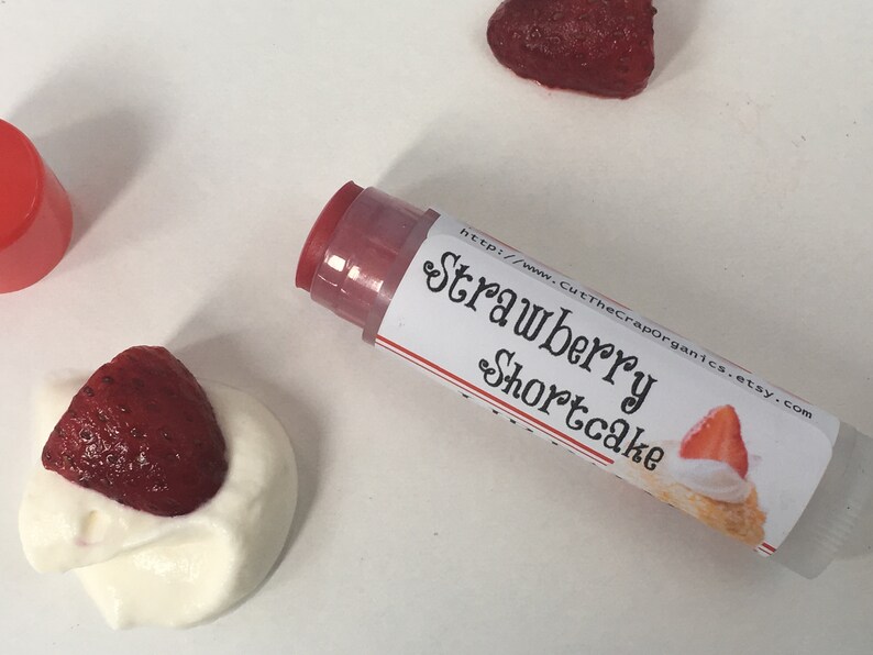 May include: A clear tube of lip balm with a red cap and a white label that says "Strawberry Shortcake" and a website address. The label also features a small illustration of a strawberry shortcake dessert.