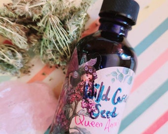 Può includere: Una bottiglia di vetro scuro con un contagocce e un'etichetta che recita "Wild Carrot Seed Queen Anne's Lace". La bottiglia è appoggiata su una superficie a righe con un cristallo rosa e un fiore secco.
