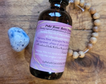 May include: A brown glass bottle with a black dropper, labeled "Poke Root/ Berry Tincture." The label is pink and purple. A blue and white stone and a wooden bead bracelet are next to the bottle. The text on the label includes directions and warnings.