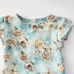 May include: A light blue short-sleeved dress with a floral print. The dress has a round neckline and a relaxed fit.
