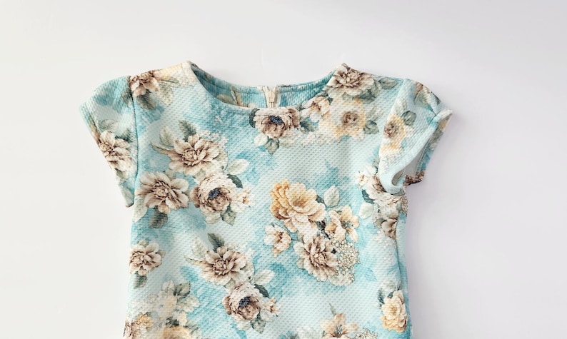 May include: A light blue short-sleeved dress with a floral print. The dress has a round neckline and a relaxed fit.
