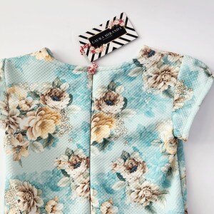 May include: A light blue dress with a floral print. The dress has short sleeves and a round neckline. The dress is made of a soft, comfortable fabric.