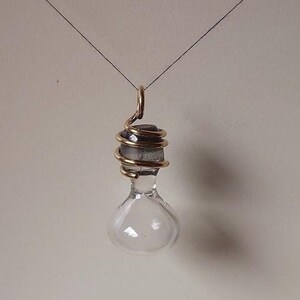May include: A clear glass pendant with gold wire wrapped around the top. The pendant is hanging from a thin black string.