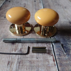 May include: Two brass door knobs with a yellow ceramic finish. The knobs are shown with the mounting hardware, including a screw and an Allen wrench.