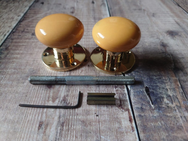 May include: Two brass door knobs with a yellow ceramic finish. The knobs are shown with the mounting hardware, including a screw and an Allen wrench.