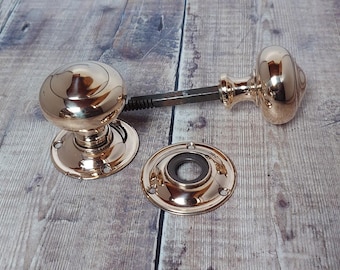 May include: A set of antique brass door knobs with a matching backplate. The knobs are round with a polished finish, connected by a metal spindle. The backplate is also brass, with a circular design and screw holes.