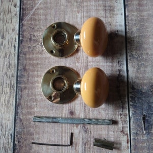 May include: Two brass door knobs with a yellow ceramic finish, a metal screw, an allen wrench, and a metal connector.