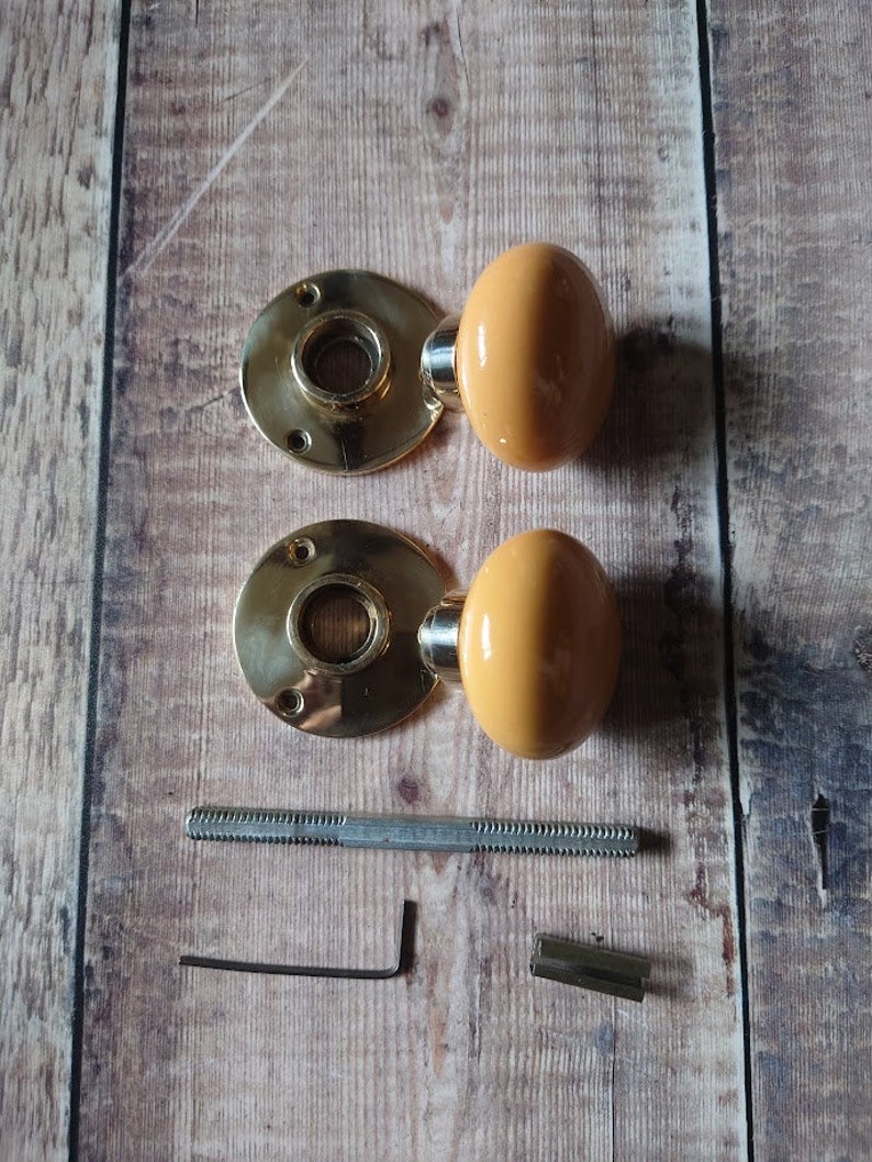 May include: Two brass door knobs with a yellow ceramic finish, a metal screw, an allen wrench, and a metal connector.