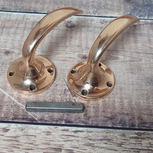 May include: Two antique copper door handles with a rounded design and a decorative base. The handles are on a wooden surface.