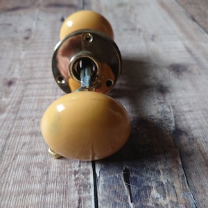 May include: A pair of yellow ceramic door knobs with a brass backplate and keyhole.