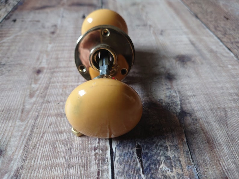May include: A pair of yellow ceramic door knobs with a brass backplate and keyhole.