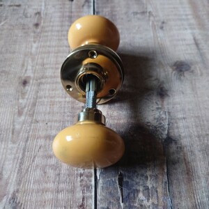 May include: A yellow ceramic door knob with a brass base and a metal spindle.