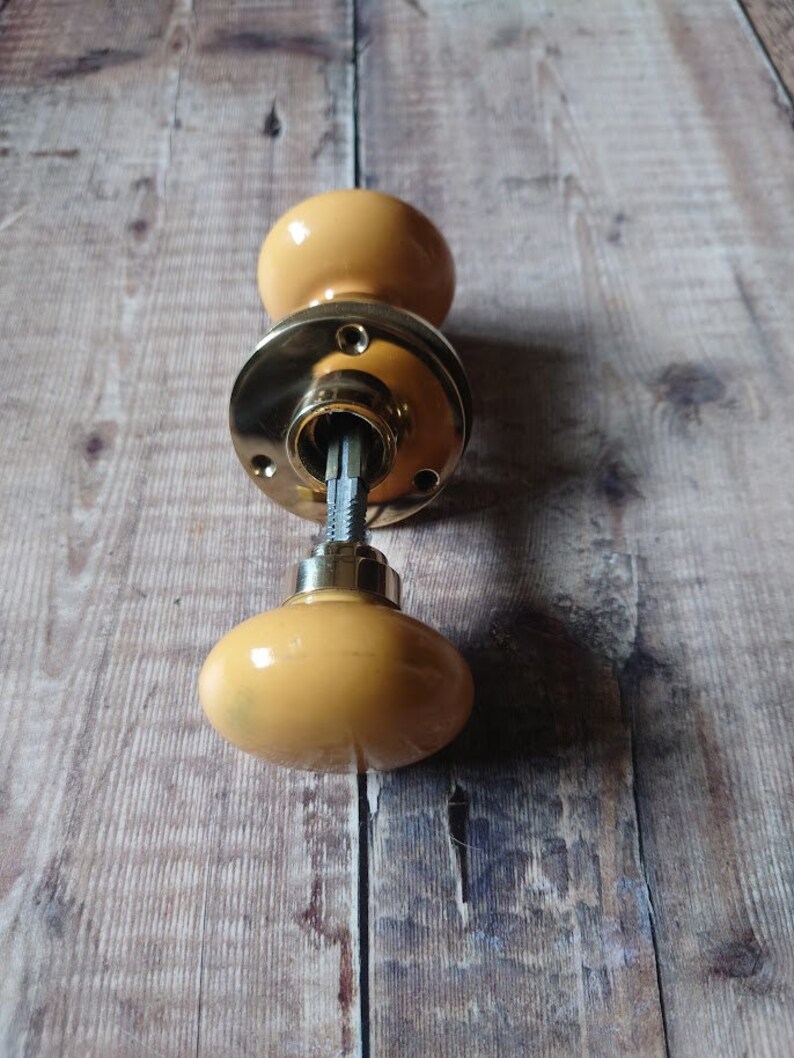 May include: A yellow ceramic door knob with a brass base and a metal spindle.