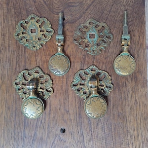 May include: Antique brass drawer pulls and backplates. The hardware features ornate floral designs and a distressed finish. The pulls have round handles and threaded posts for mounting. The backplates have a square center.