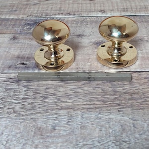 May include: Two gold door knobs with round bases. The knobs are on a wooden surface.