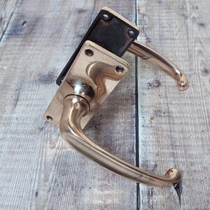 May include: A brass door handle with a square backplate and a curved lever. The handle is in a polished finish.