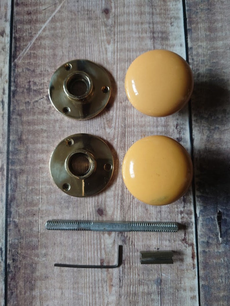 May include: A set of two yellow ceramic door knobs with brass backplates, a screw, an allen wrench, and a metal plate.