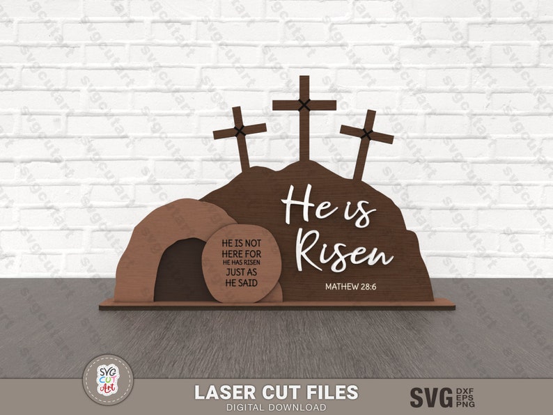 May include: A laser cut wooden Easter cross and tomb design with the text "He is Risen" and a scripture reference. The tomb has a sign that reads "He is not here for he has risen just as he said."