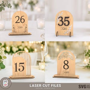Peut inclure: Quatre panneaux de table en bois en forme d'arche avec des motifs découpés au laser. Les panneaux affichent les chiffres 26, 35, 15 et 8, avec le mot Table imprimé sous chaque chiffre. Chaque panneau repose sur une base en bois plate.