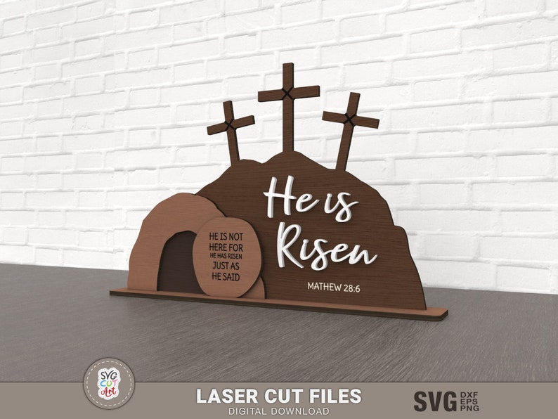 May include: A laser cut wooden Easter sign with three crosses and a tomb. The sign reads "He is Risen" with the scripture reference "Mathew 28:6". The tomb has a sign that reads "He is not here for He has risen just as He said."