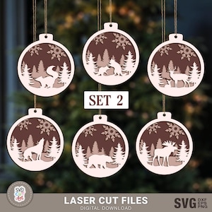 May include: Set of six laser cut Christmas ornament designs featuring winter scenes with animals. The ornaments are brown with white snowflakes and animals. The designs include a fox, a wolf, a deer, a bear, and a moose.